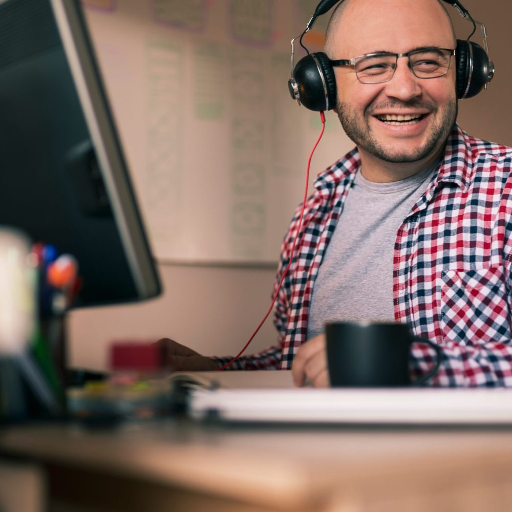Male web designer sitting at his desk in an office, wearing headset and working; freelancer working from home